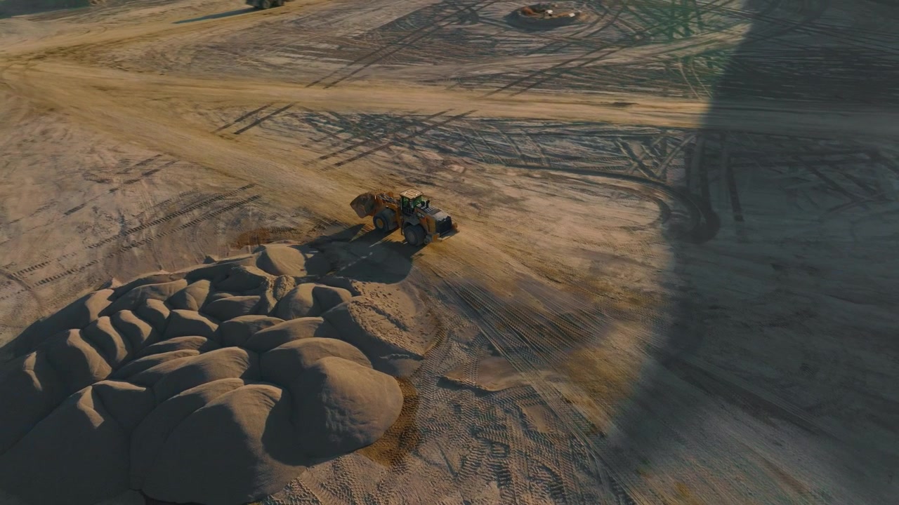 Aerial view of earthmover working in a gravel pit in Utah, casting a long shadow in the afternoon sun. tracking shot