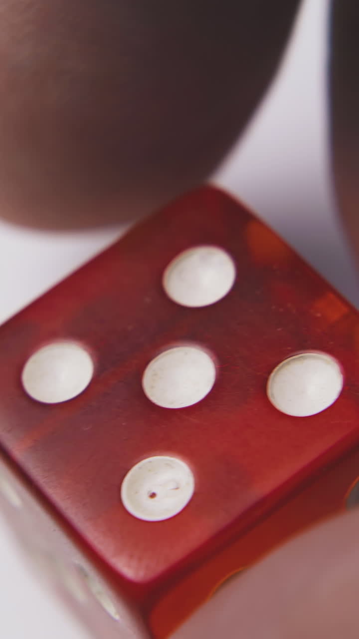 young man turns bright red plastic dice with symbols five of spots on sides in white background extreme close view
