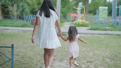 a pregnant mother and her young daughter enjoy playful time together at a playground in the park, surrounded by trees and greenery