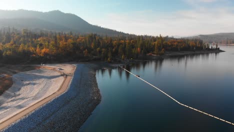 aerial shot of a dam on a blue alpine lake surrounded by pine trees and mountains