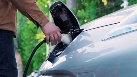 proceso de reabastecimiento de combustible de un automóvil eléctrico. un disparo debajo de la escotilla donde se carga el automóvil ecológico eléctrico. la escotella de carga del automóvil eléctrico se abre automáticamente. una mano masculina inserta un automóvil erecto