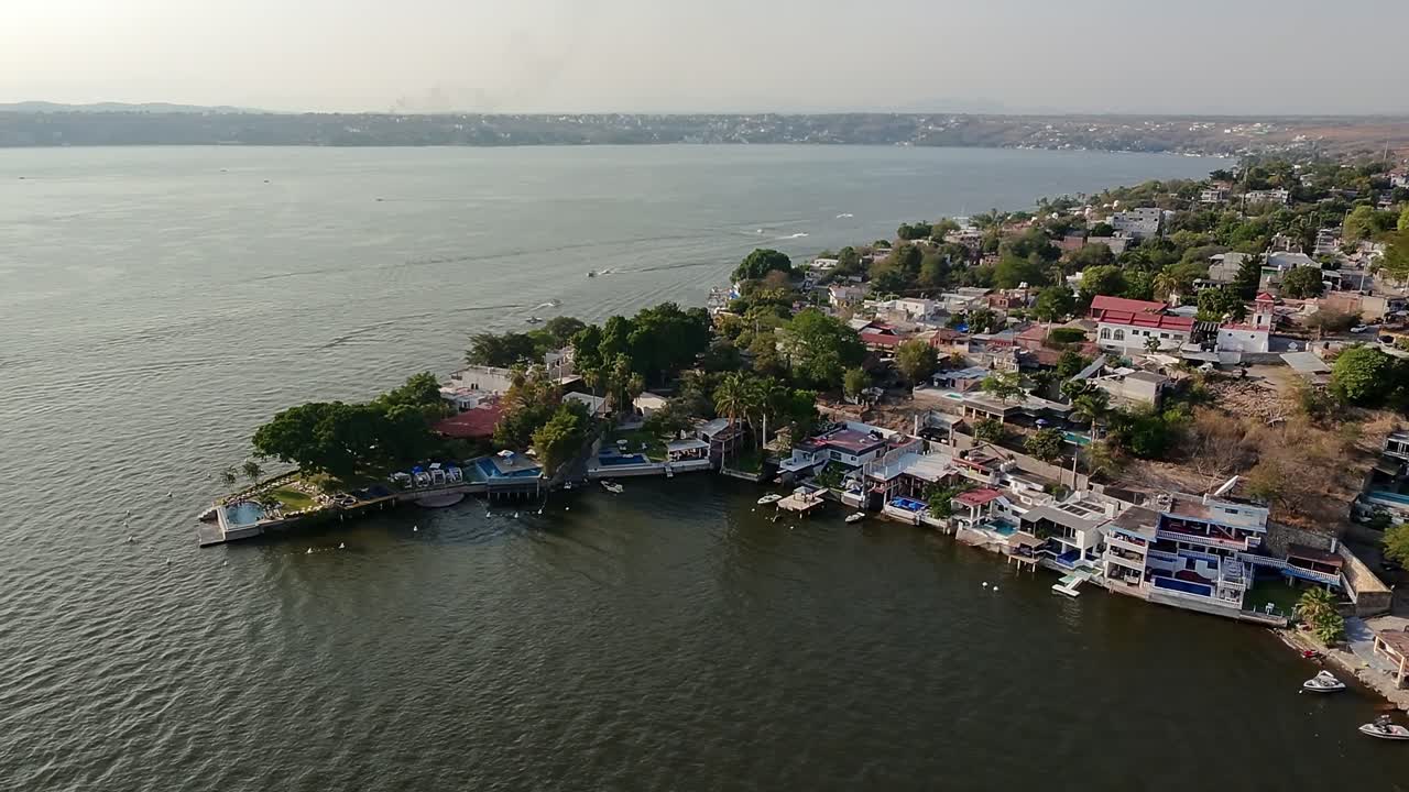 Semi orbit aerial shot of lakefront properties and lush trees on the shore of Tequesquitengo lake in daylight.