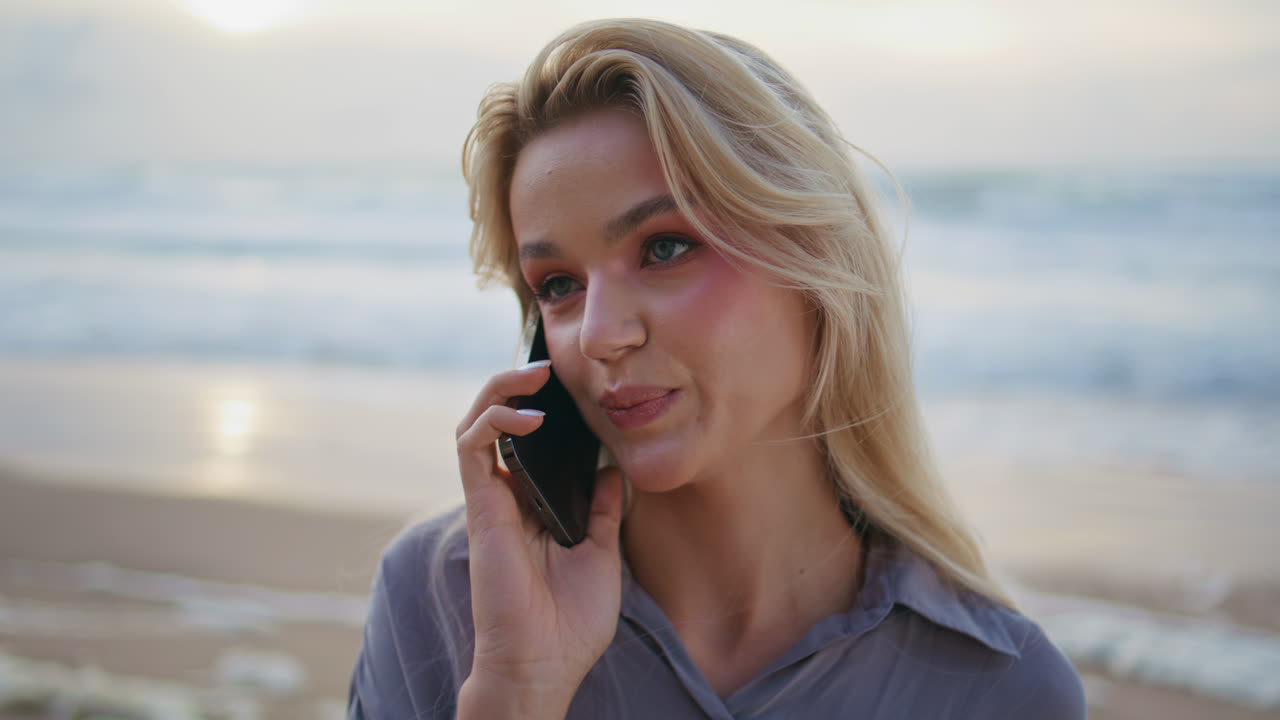 una mujer de vacaciones contestando una llamada en el océano al atardecer.
