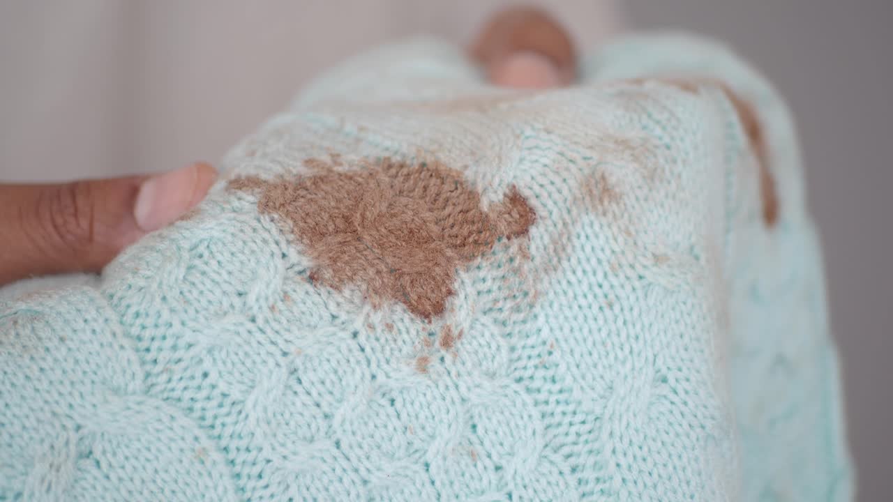 Detailní záběr ruky držící zašpiněný modrý pletený svetr