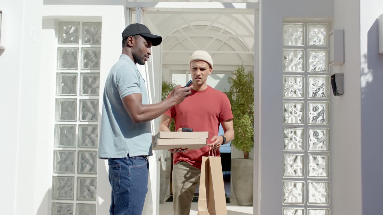 Male African American delivery person on porch handing pizzas while customer tapping reader paying