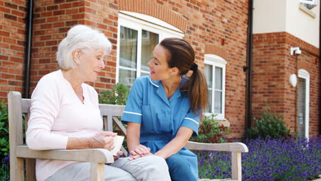 Senior-Woman-Sitting-On-Bench-And-Talking-With-Nurse-In-Retirement-Home