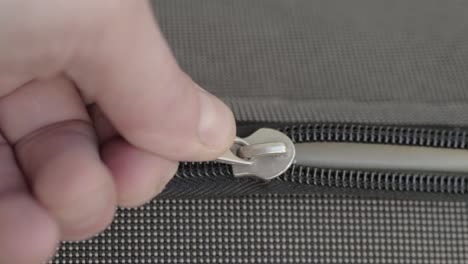 Hand-pulling-metal-zip-to-open-suitcase-luggage-close-up-macro