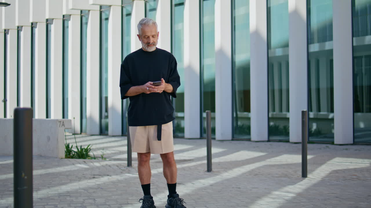 Uomo in pensione che digita sullo smartphone in centro. Uomo maturo pensieroso che usa il cellulare