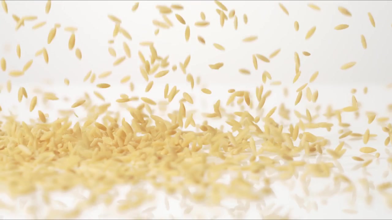 Orzo secco non cotto che rimbalza su un tavolo bianco al rallentatore in primo piano macro prima di posarsi.
