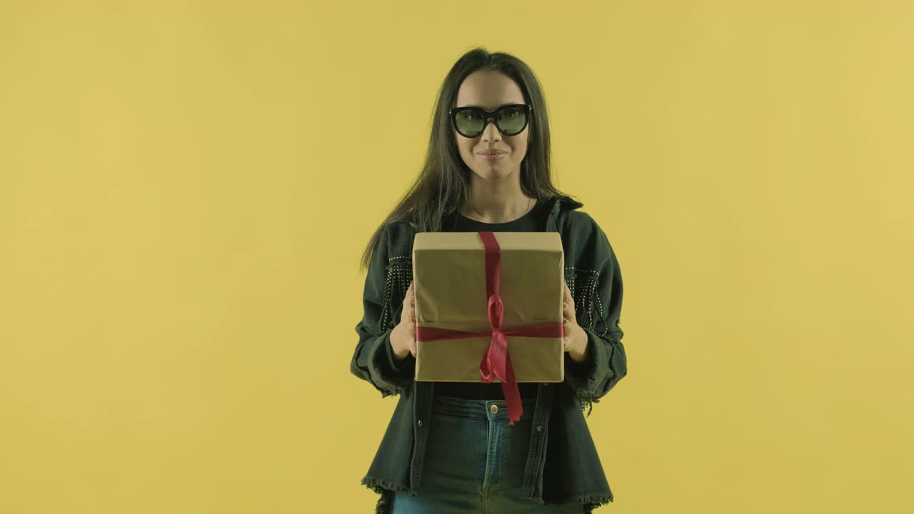 chica feliz con una caja de regalos y mirando a la cámara sobre un fondo amarillo