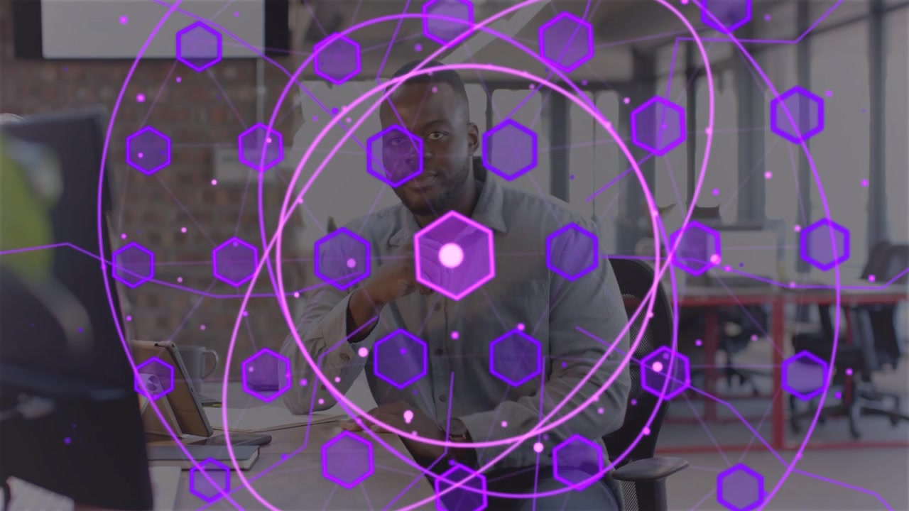 Typing worker wearing watch at shared desk using tablet, purple marker forming HUD reviewing data