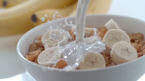 leche vertiendo en un cuenco de cereales y plátanos en cámara lenta
