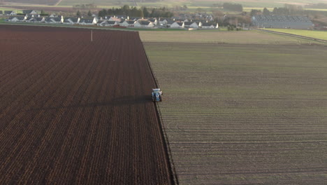 Aerial-view-of-a-farm-tractor-ploughing-a-field-in-Aberdeenshire-on-a-sunny-day,-Scotland