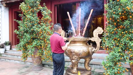 man lighting incense sticks at temple entrance