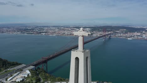 aerial drone shot circling around christ the king statue and lisbon bridge with aeroplane flying in the background