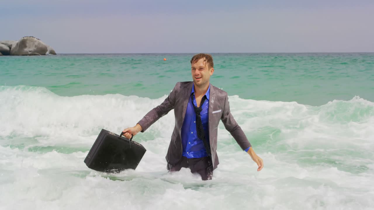 vista frontal de un hombre de negocios caucásico caminando con un maletín en el mar en la playa 4k