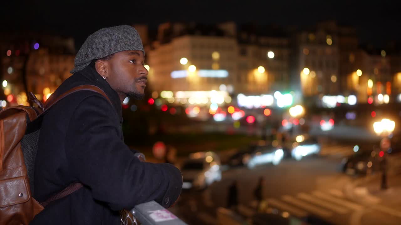 A man with a backpack looking at city lights at night