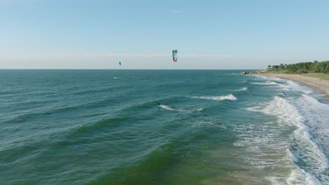 establecimiento de una vista aérea de un grupo de personas dedicadas al kitesurf, día soleado de verano, olas altas, deportes extremos, playa de karosta en el mar báltico, amplia toma de avión no tripulado avanzando