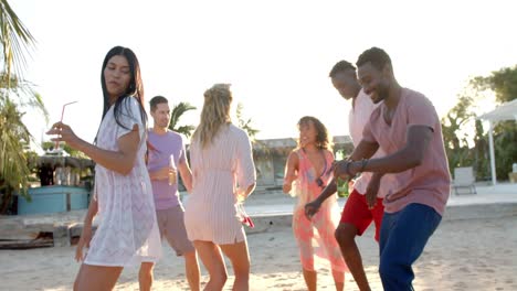 happy diverse group of friends dancing holding cocktails at beach