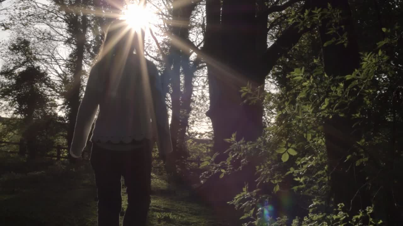 Woman walking into woodland with lens flare at sunset medium shot