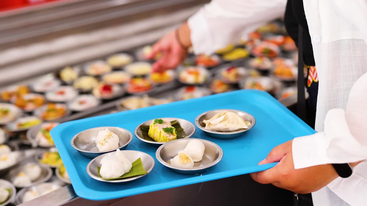 A vendor serves a variety of dim sum on a blue tray in a bustling Phuket market, captured with vibrant lighting