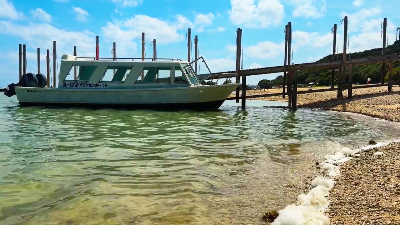 Molo in legno con barca turistica dal fondo di vetro ormeggiata alla spiaggia di Mibaru a Nanjo, Okinawa, Giappone. Inquadratura statica