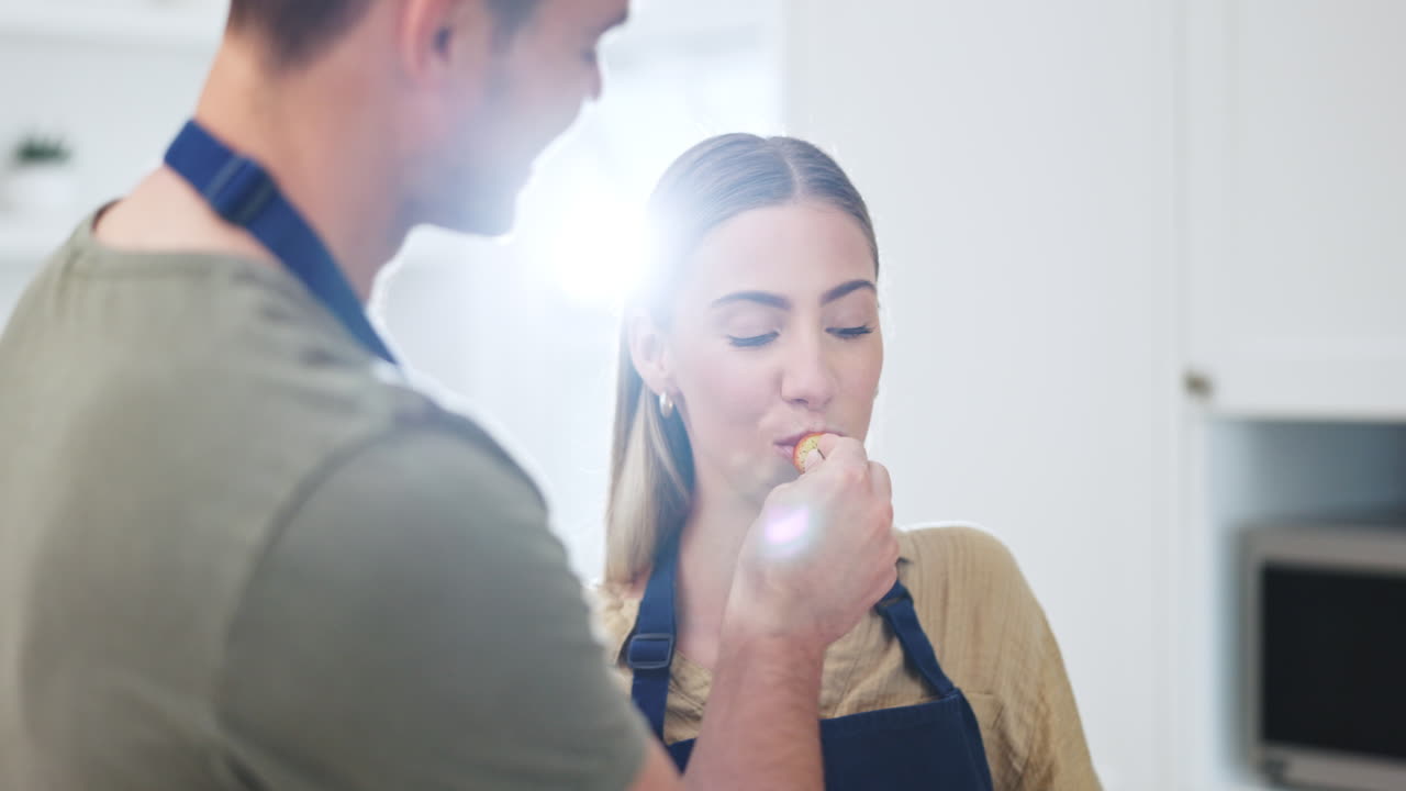 pareja, delantal y alimentación de frutas en la cocina del hogar