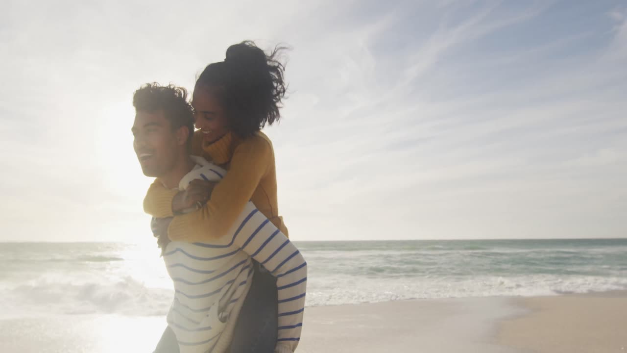 Happy hispanic man carrying piggyback woman and having fun on beach
