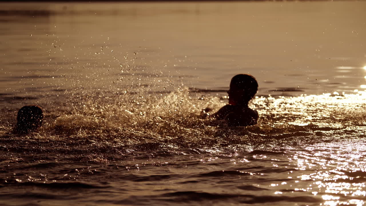Silhouette of boy splashing water in the river. Evening background and two boys playing in the water happily. Healthy childhood.