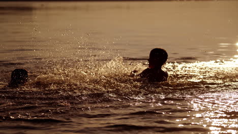 silhouette of boy splashing water in the river. evening background and two boys playing in the water happily. healthy childhood.