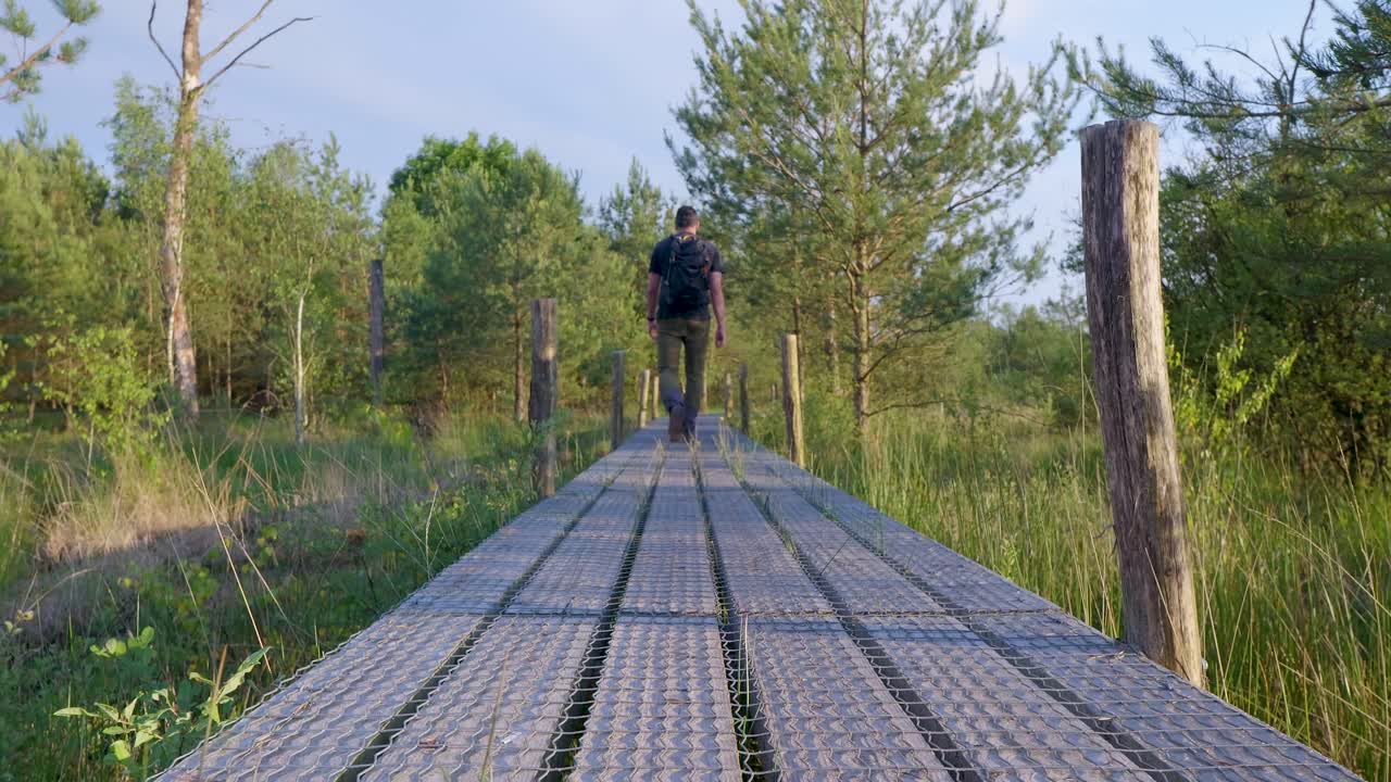 Uomo in escursione su una passerella di legno attraverso una palude boschiva