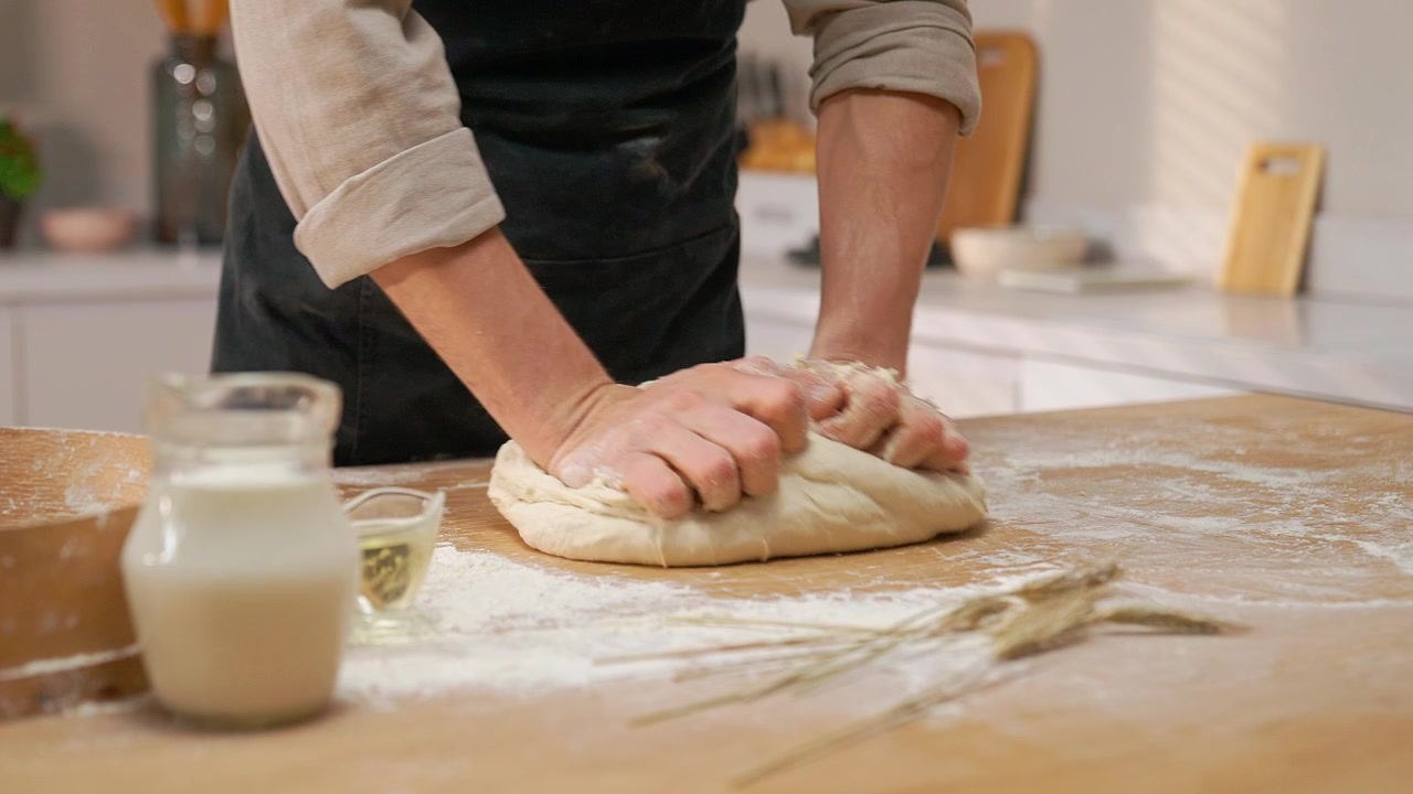 Close-up of Baker's Hands Kneading Dough on a Floured Wooden Table