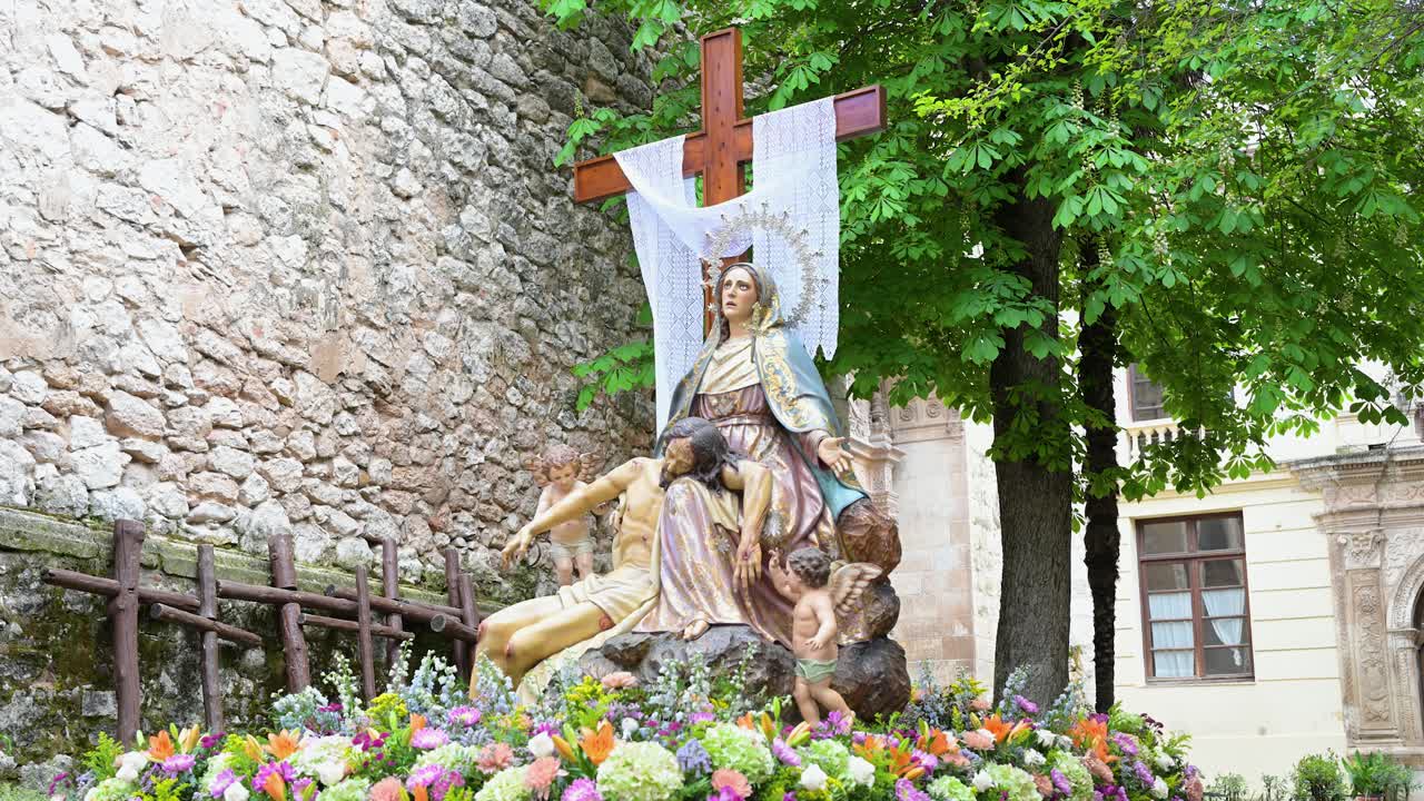 A vibrant cultural display in Guadalajara, Spain: An ornate Pietà float, adorned for Easter, awaits. It vividly showcases centuries of Spanish religious artistry, tradition, and fervent devotion.