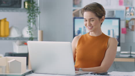 Female-Architect-In-Office-Making-Video-Call-At-Desk-On-Laptop