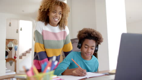 Happy-african-american-mother-and-son-waving-to-camera-on-laptop-in-kitchen,-slow-motion