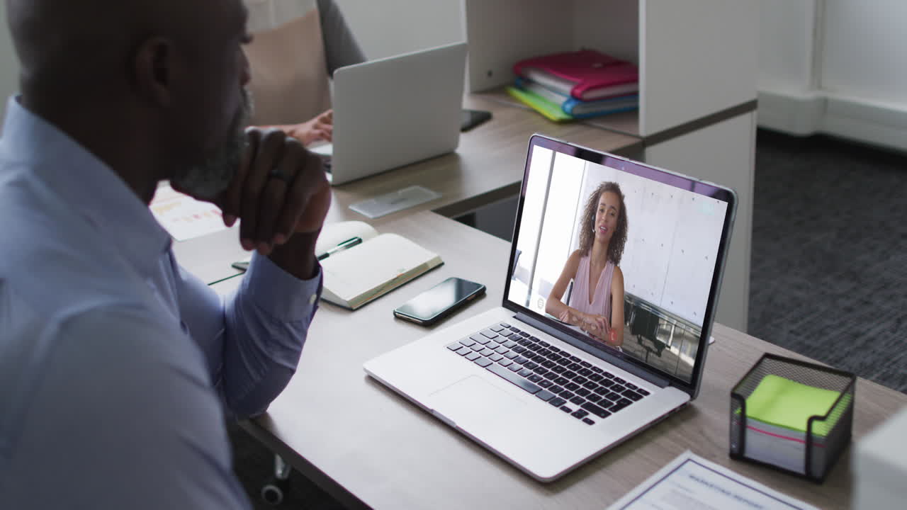 African american businessman sitting at desk using laptop having video call with female colleague