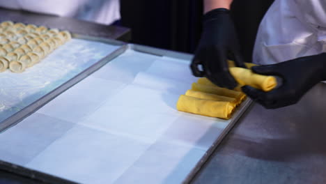 hands in black latex gloves put the rolled crepes with stuffing on a tray. preparing fresh food at restaurant. close up.