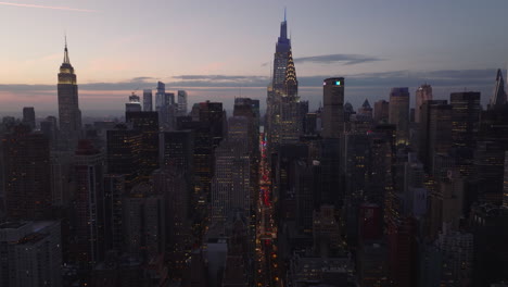 Forwards-fly-above-city-at-dusk.-Illuminated-iconic-high-rise-buildings-Chrysler-and-Empire-State-Building.-Manhattan,-New-York-City,-USA