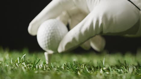 close up of hand with glove holding golf ball on grass and black background, copy space, slow motion