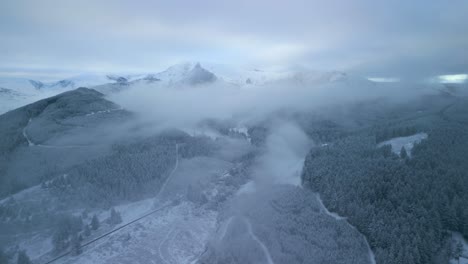 emerging from low cloud over snowy winter forest and mountain landscape