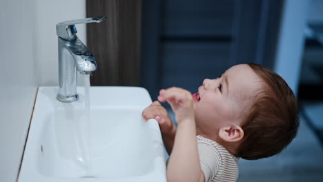 curious little caucasian toddler plays with water. kid opens the faucet letting water flow.