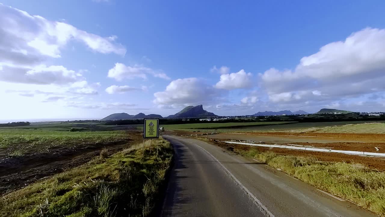 Amazing car perspective showcasing Mauritius's dramatic mountain peaks contrasting with lush sugar cane plantations in the foreground. Perfect for travel and tourism content.