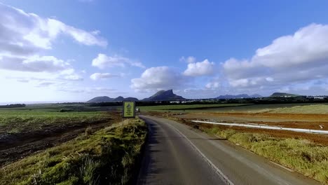 amazing car perspective showcasing mauritius's dramatic mountain peaks contrasting with lush sugar cane plantations in the foreground. perfect for travel and tourism content.