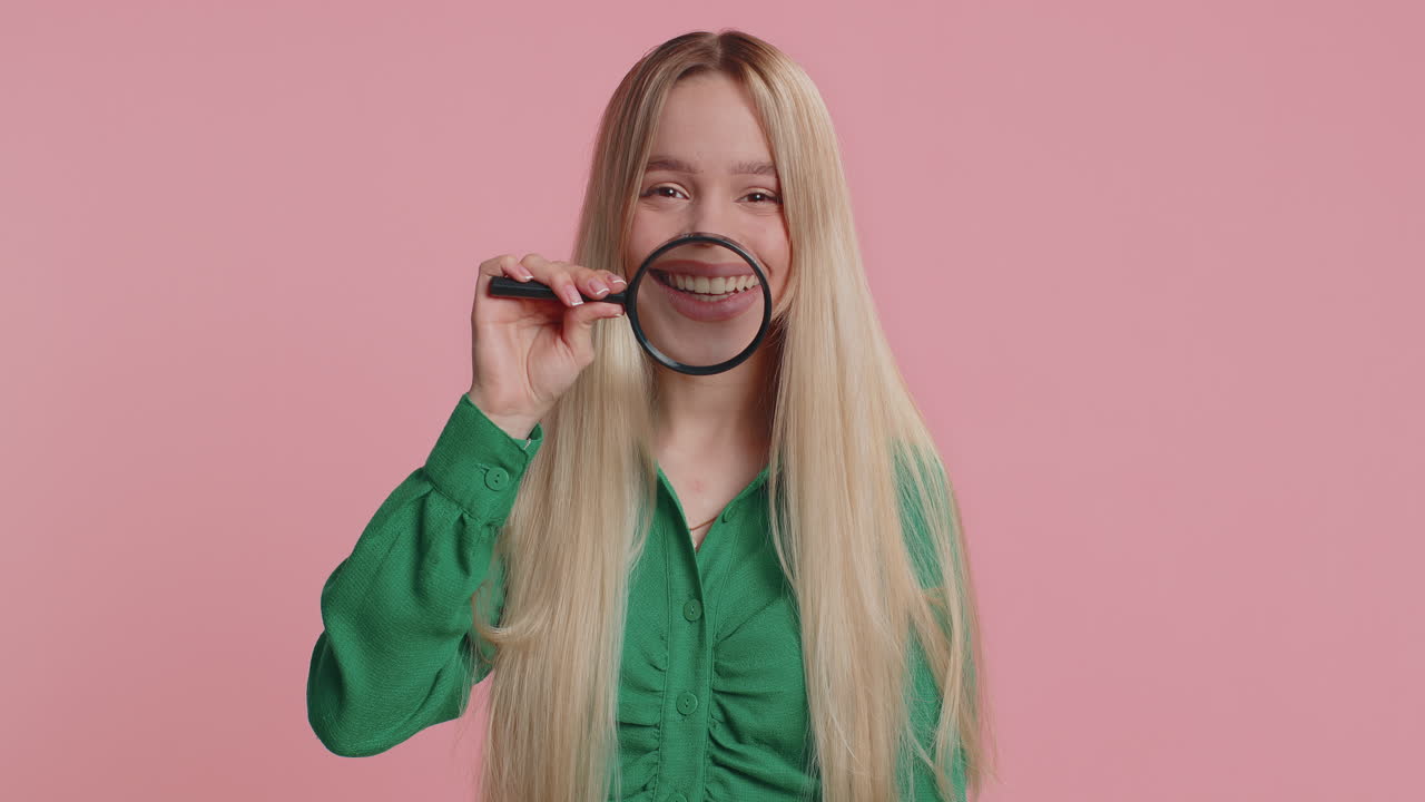 Caucasian woman holding magnifier glass on teeth looking at camera showing funny smiling face mouth