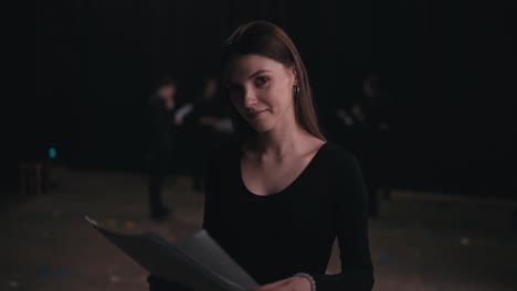 Portrait-of-a-confident-girl-actor-in-a-black-suit-who-revises-her-text-and-script-of-the-work-during-a-rehearsal-and-preparation-for-a-performance-on-stage-in-the-theater