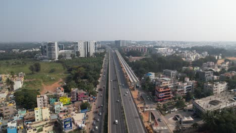 aerial view of a rapidly developing indian highway featuring a service road, fast-moving cars, and the construction of a metro train bridge