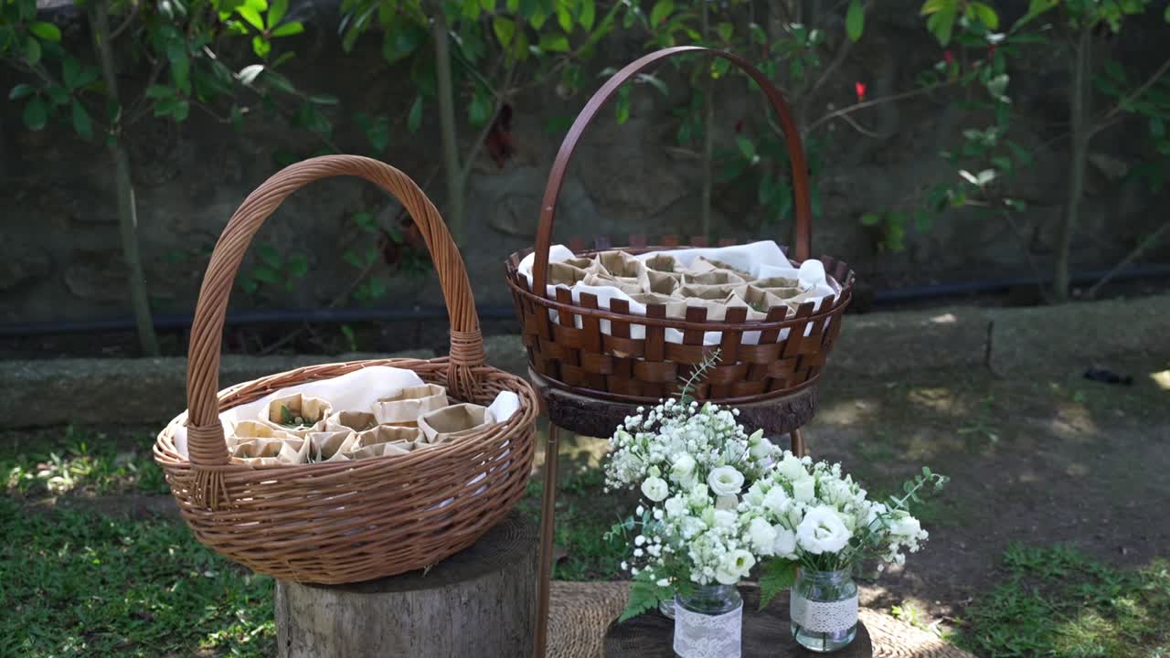 花柄の瓶の横に置かれた、オリーブの葉が入った紙コーンを持つ枝編みバスケット