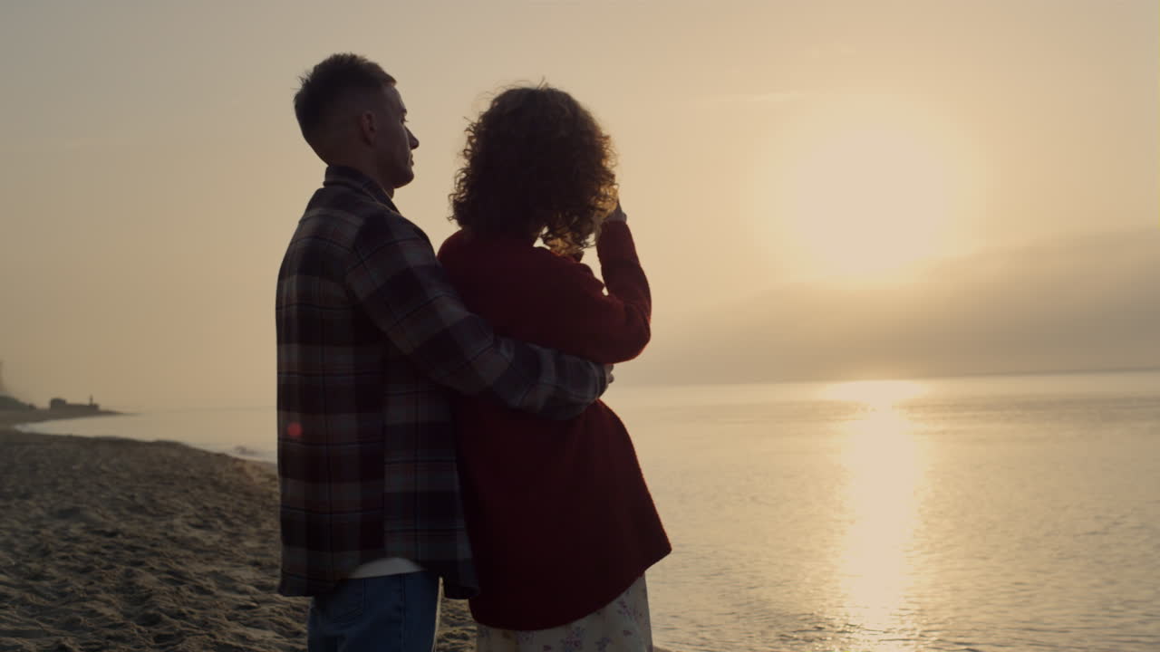Man embracing woman on beach at sunrise. Girl making photo of sea landscape