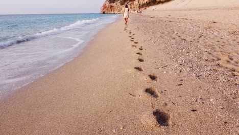 woman leaves footprints during walk on milos beach, lefkada island, greece - aerial reveal