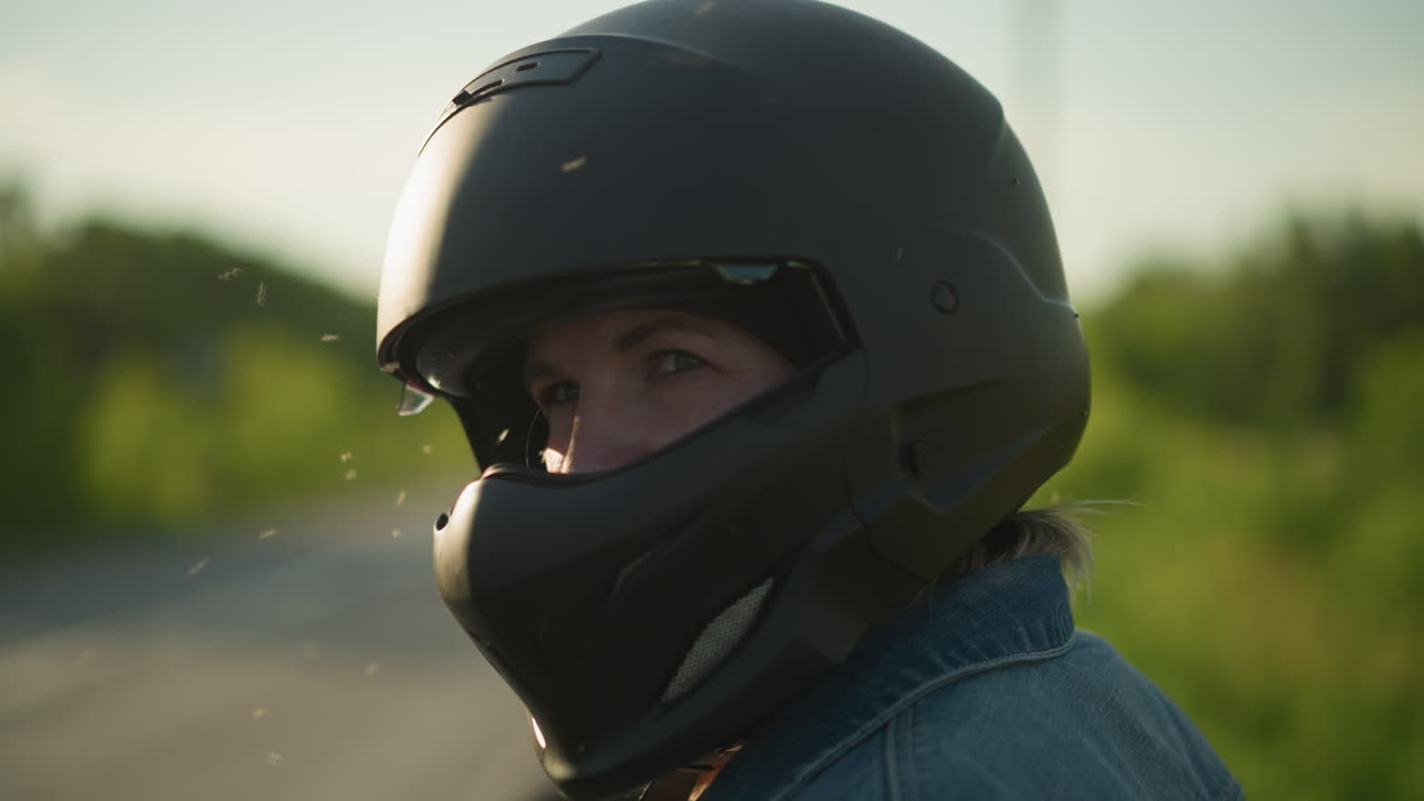 Close-up side view of a woman wearing a matte black helmet, looking contemplatively ahead, a small flying insect is visible near her face